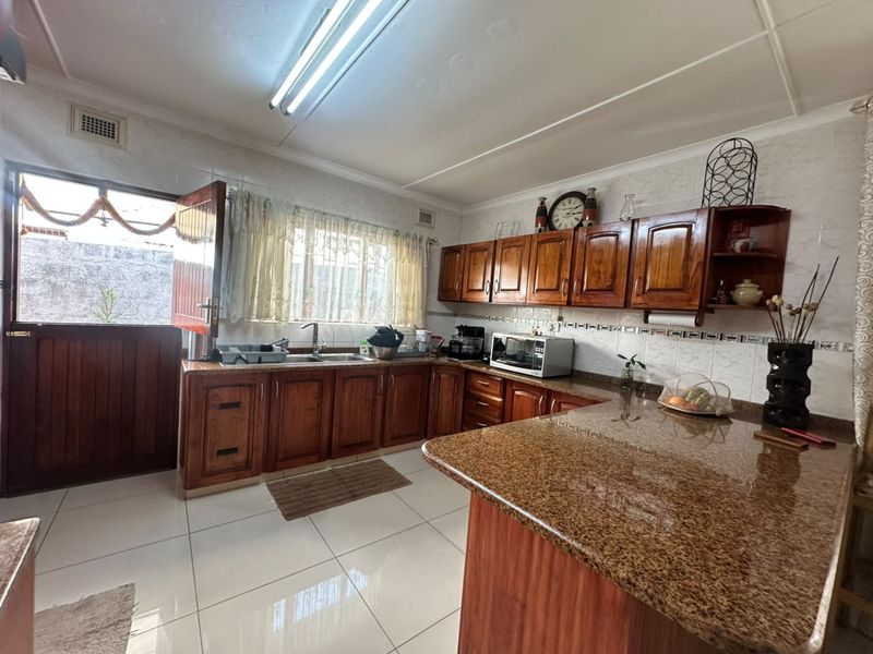A functional kitchen featuring warm-toned wooden cabinetry, granite countertops, tiled flooring, and a stable door providing direct access to the exterior.