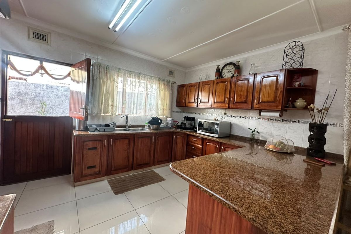 A functional kitchen featuring warm-toned wooden cabinetry, granite countertops, tiled flooring, and a stable door providing direct access to the exterior.