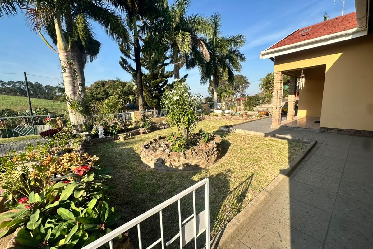 A well-maintained rear garden featuring a tiled patio, brick pillars, and established landscaping with mature palm trees and stone garden beds.