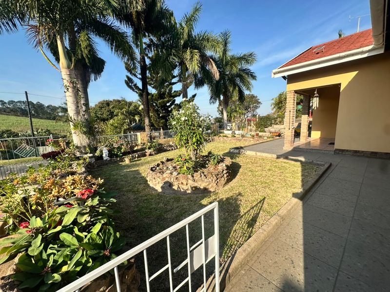 A well-maintained rear garden featuring a tiled patio, brick pillars, and established landscaping with mature palm trees and stone garden beds.