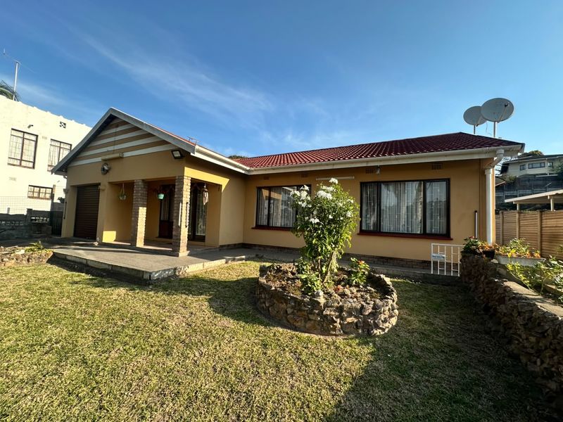 Front elevation of a single-story house featuring a tiled roof, covered porch, and a landscaped front garden with a stone-walled flower bed.