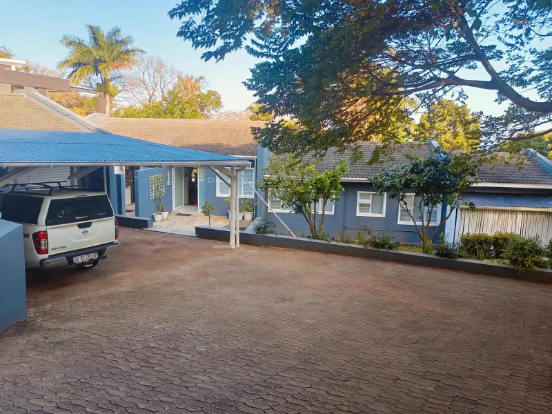 Front exterior view of the property featuring a paved driveway, covered carport, and blue-painted facade with tiled roofing.