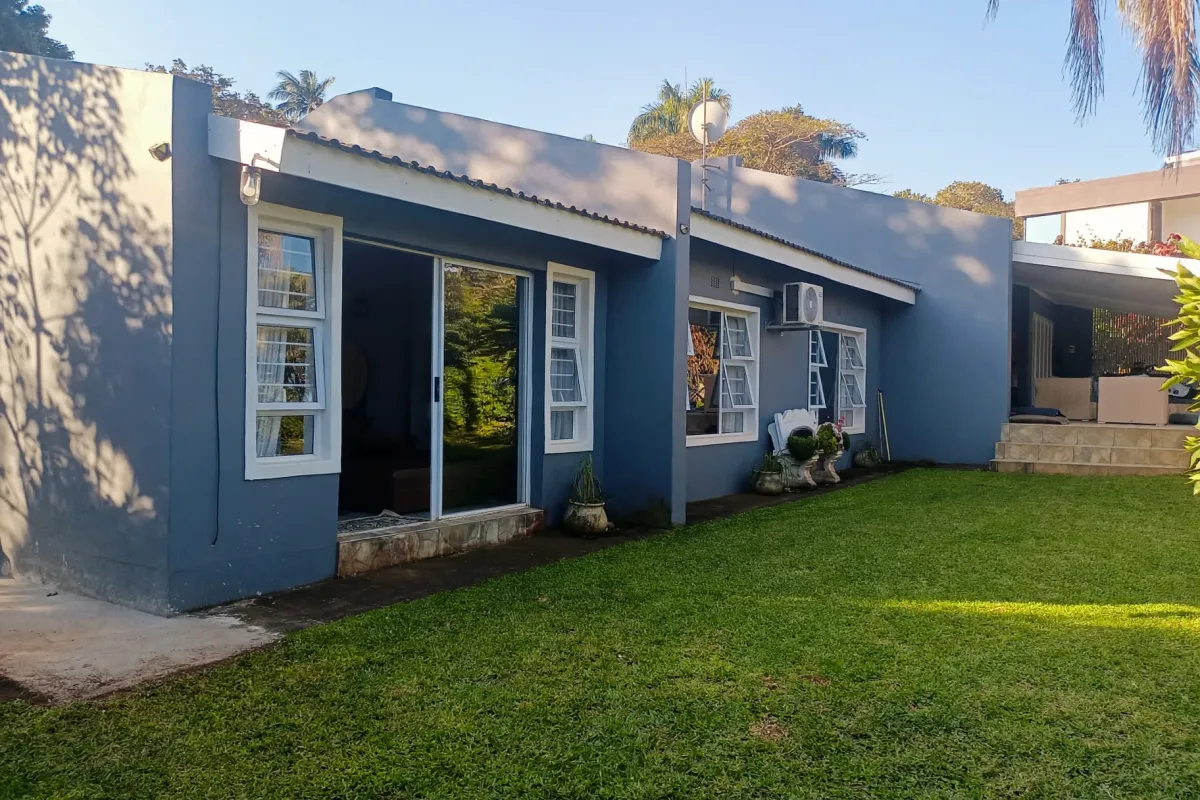 Rear view of the property featuring a blue painted facade, sliding glass doors, casement windows, an air conditioning unit, and a well-maintained lawn.