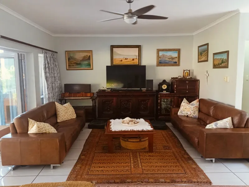 A well-maintained living room featuring tiled flooring, a central ceiling fan, and large sliding glass doors providing natural light and outdoor access.