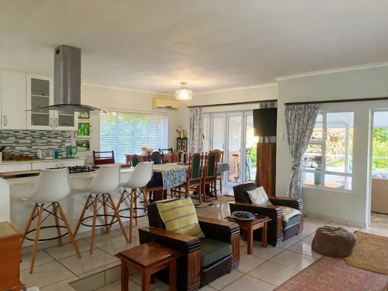 Spacious open-plan living area featuring a modern kitchen with island, tiled floors, and seamless access to the outdoor patio through sliding glass doors.