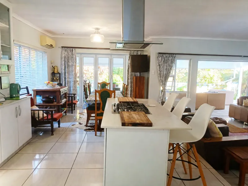 Spacious open-plan living and kitchen area featuring a central island with gas hob, tiled flooring, and large sliding doors leading to the outdoor space.