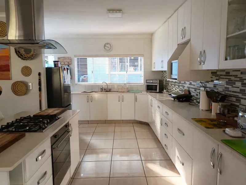 A well-maintained kitchen featuring white cabinetry, a gas hob, built-in oven, stainless steel extractor fan, and a mosaic tile backsplash.