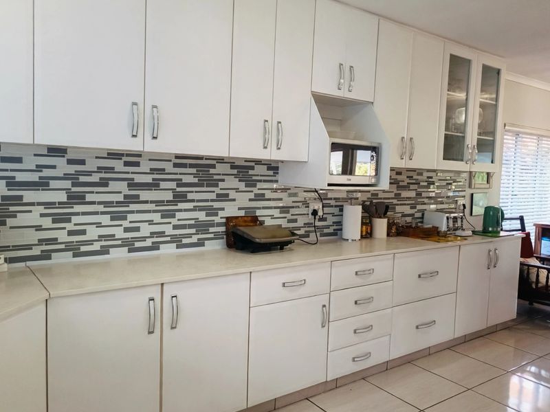 A functional kitchen featuring white cabinetry, a modern tiled backsplash, stone countertops, and built-in microwave housing.