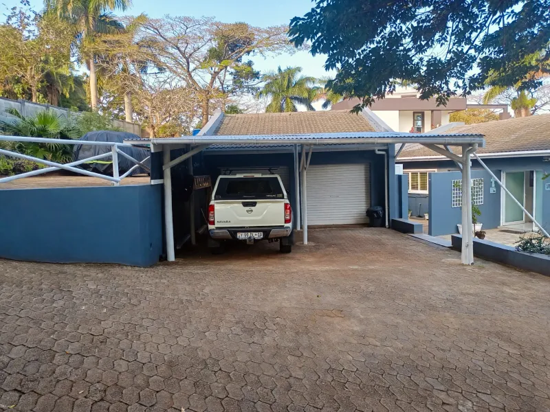 Front exterior view featuring a paved driveway, a covered carport, and a garage with a roller shutter door.