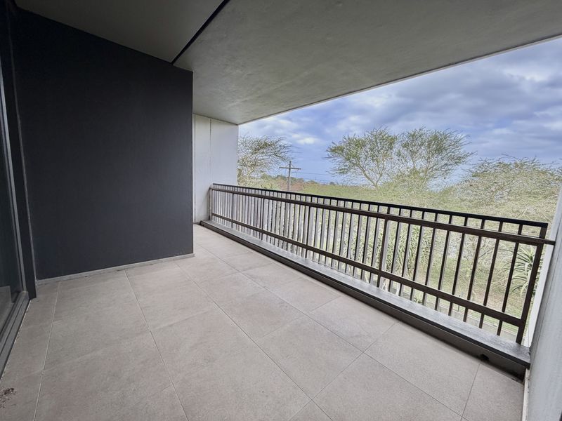 A spacious, covered balcony featuring modern tiled flooring and a secure metal balustrade, offering an open outdoor area with natural views.