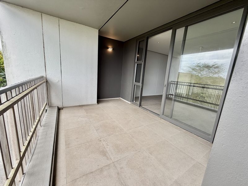 A clean, modern covered balcony featuring tiled flooring, a metal balustrade, and large sliding glass doors providing access to the interior living space.