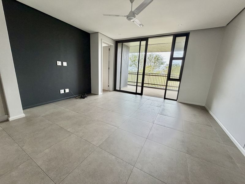 A bright, modern, and empty living room featuring large format floor tiles, a dark accent wall, and sliding doors leading to a balcony.