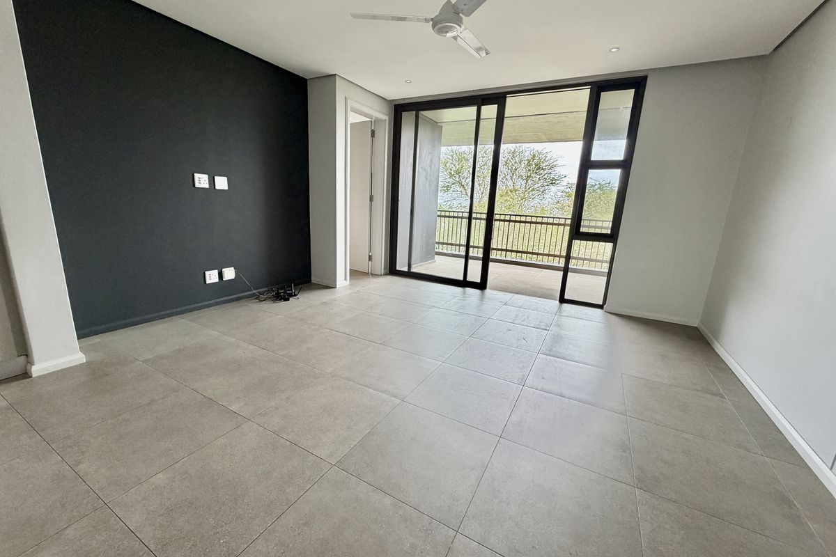 A bright, modern, and empty living room featuring large format floor tiles, a dark accent wall, and sliding doors leading to a balcony.