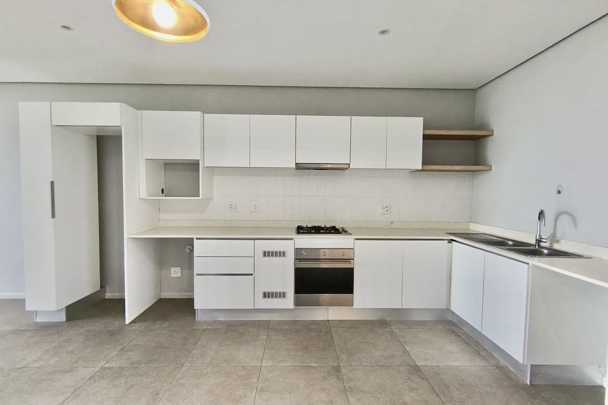 Modern, clean-lined kitchen featuring white cabinetry, stone countertops, integrated gas hob, electric oven, and a double sink with tiled flooring.
