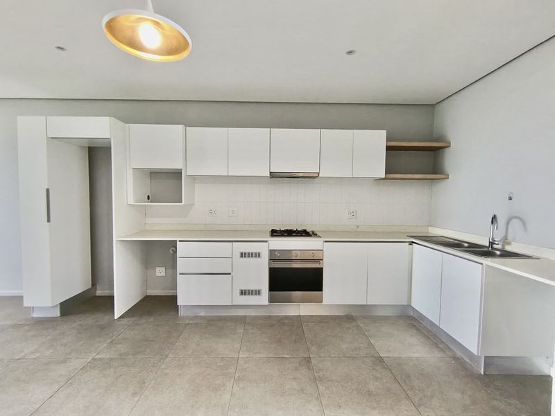 Modern, clean-lined kitchen featuring white cabinetry, stone countertops, integrated gas hob, electric oven, and a double sink with tiled flooring.