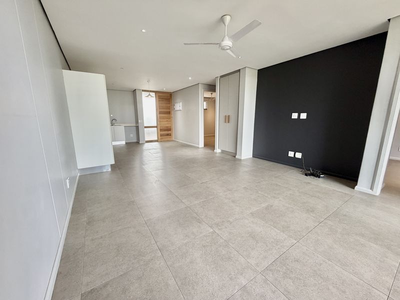 Spacious open-plan living area featuring modern large-format floor tiles, a ceiling fan, and a striking black feature wall with integrated storage.