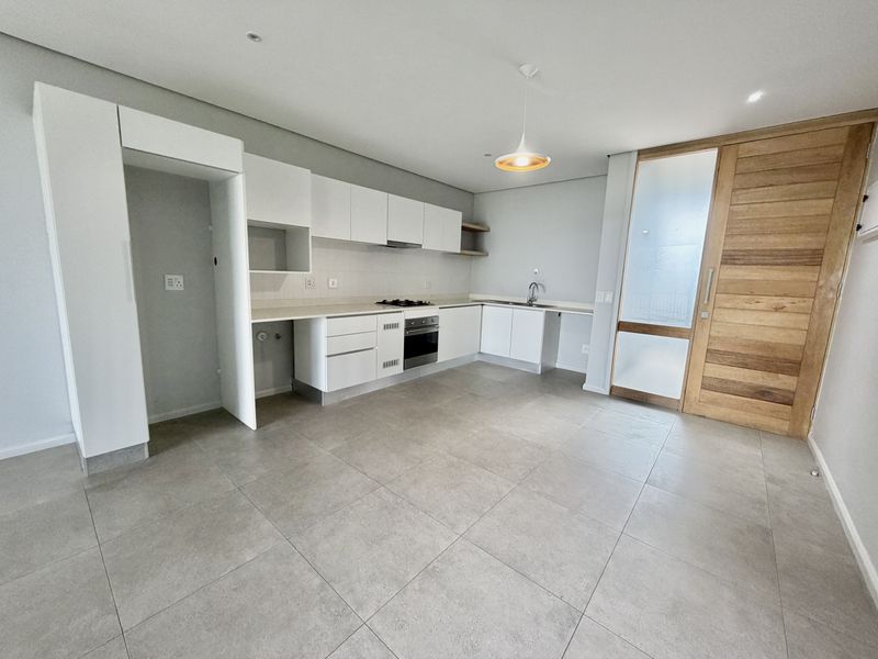 Modern kitchen featuring white cabinetry, integrated appliances, tiled flooring, and a stylish timber door, offering a clean and functional space.