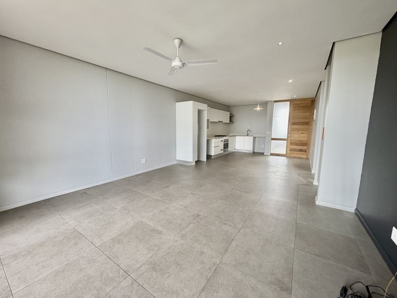 Spacious open-plan living area featuring large format floor tiles, a modern kitchen with built-in appliances, and a contemporary ceiling fan.