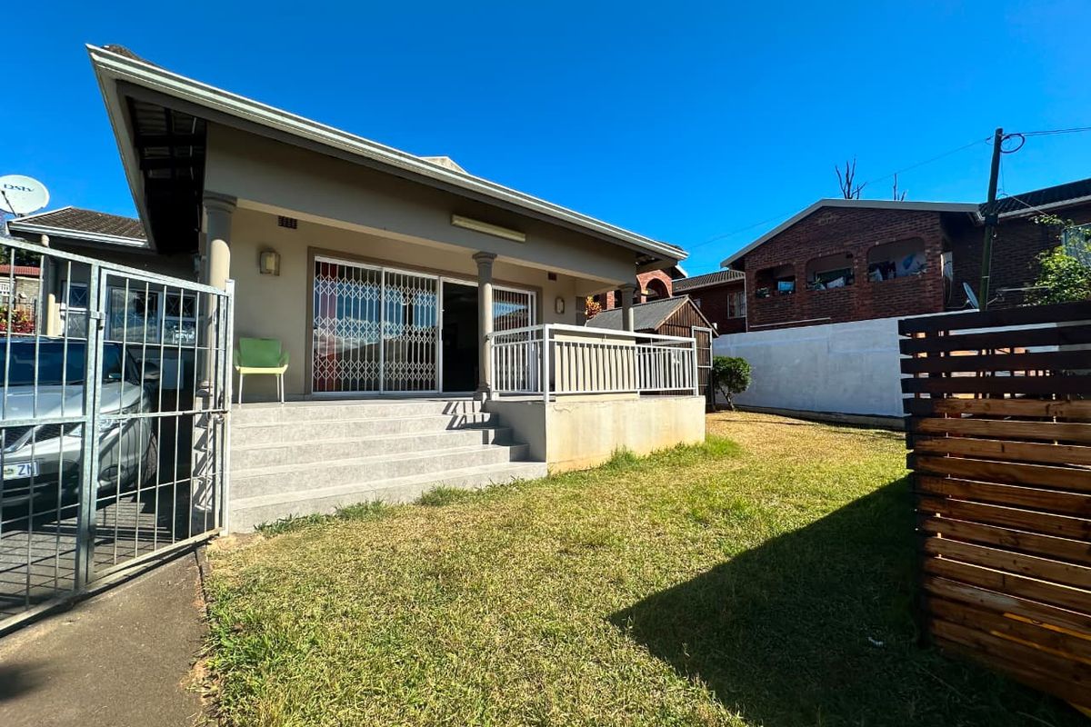Rear view of the house featuring a raised concrete patio, sliding glass doors with security gates, and a private garden area.