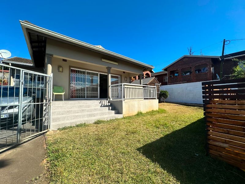 Rear view of the house featuring a raised concrete patio, sliding glass doors with security gates, and a private garden area.