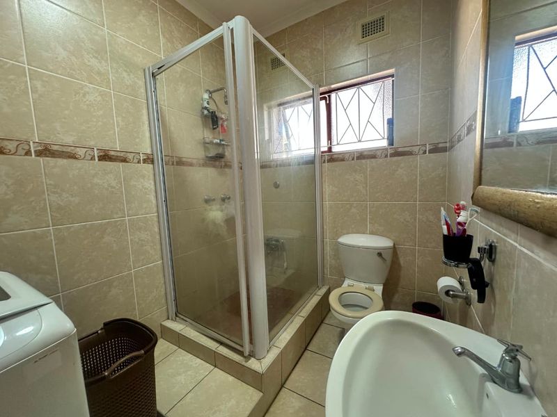 A functional bathroom featuring a tiled shower enclosure, pedestal basin, and toilet, with neutral wall and floor tiling throughout.