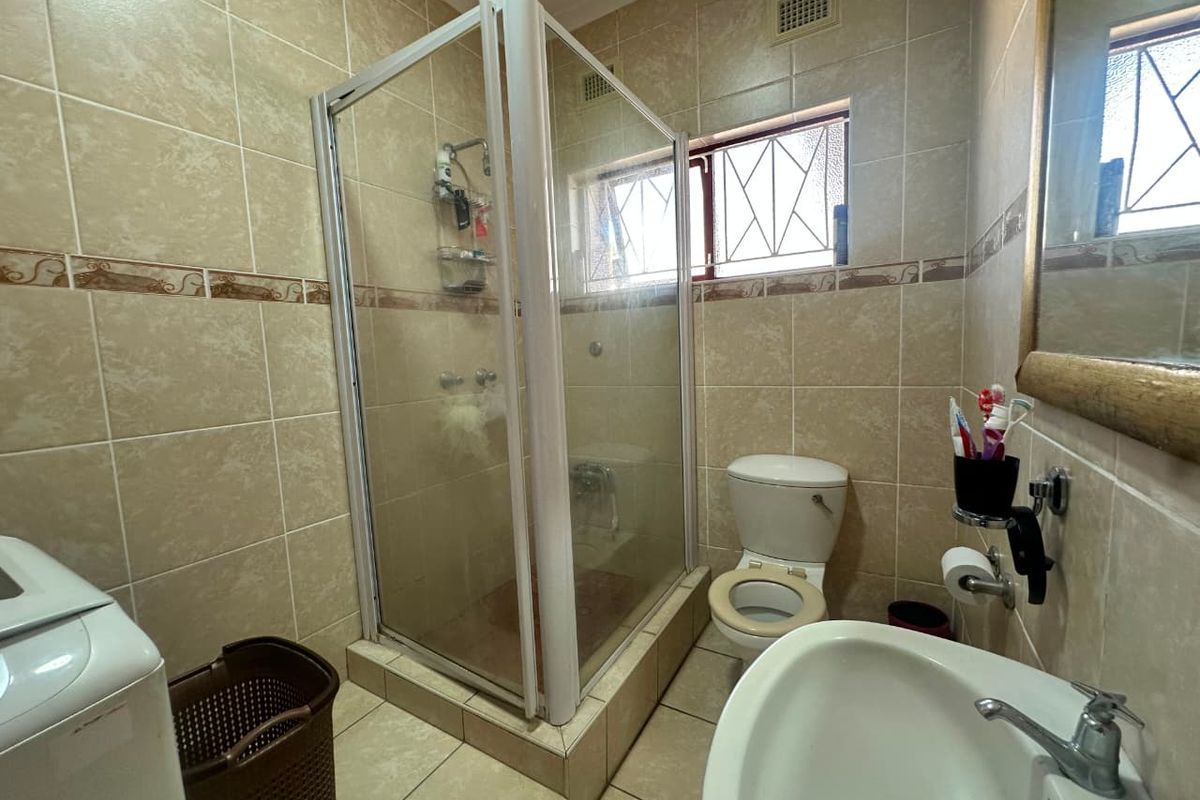 A functional bathroom featuring a tiled shower enclosure, pedestal basin, and toilet, with neutral wall and floor tiling throughout.