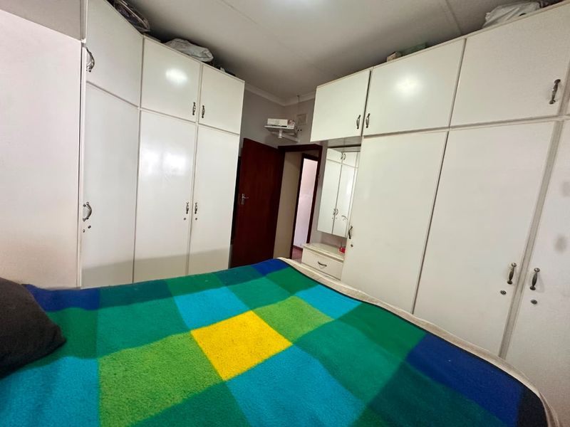 A bedroom featuring extensive white built-in cupboards with integrated vanity and mirror, providing ample storage space.