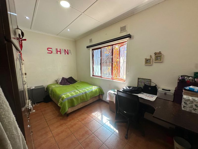 A functional bedroom featuring tiled flooring, built-in storage, and security burglar bars on the window, offering a practical space with potential for cosmetic updates.