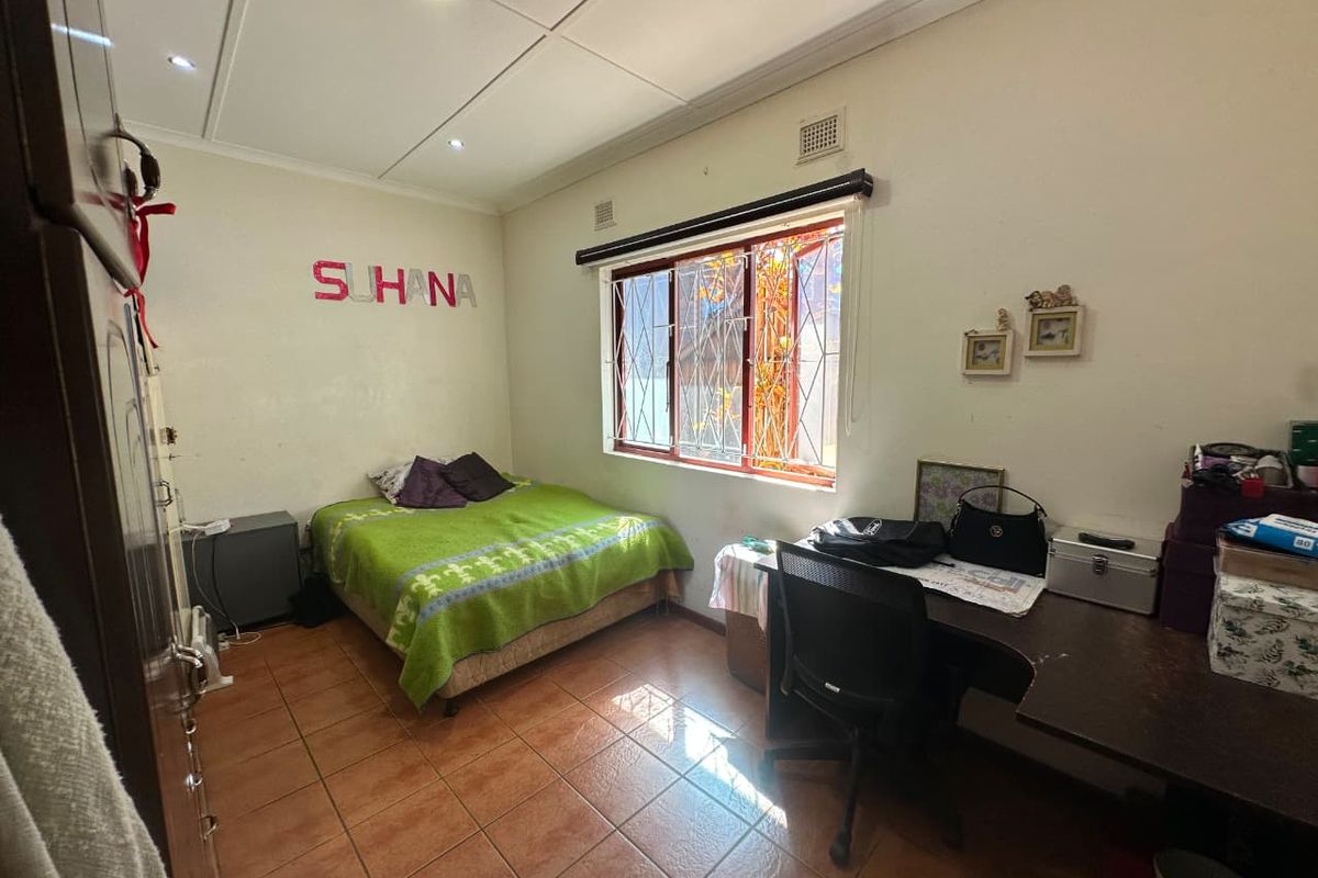 A functional bedroom featuring tiled flooring, built-in storage, and security burglar bars on the window, offering a practical space with potential for cosmetic updates.