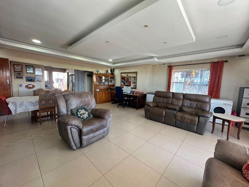 Spacious open-plan living area featuring tiled flooring, a recessed ceiling with downlights, and security bars on the windows.
