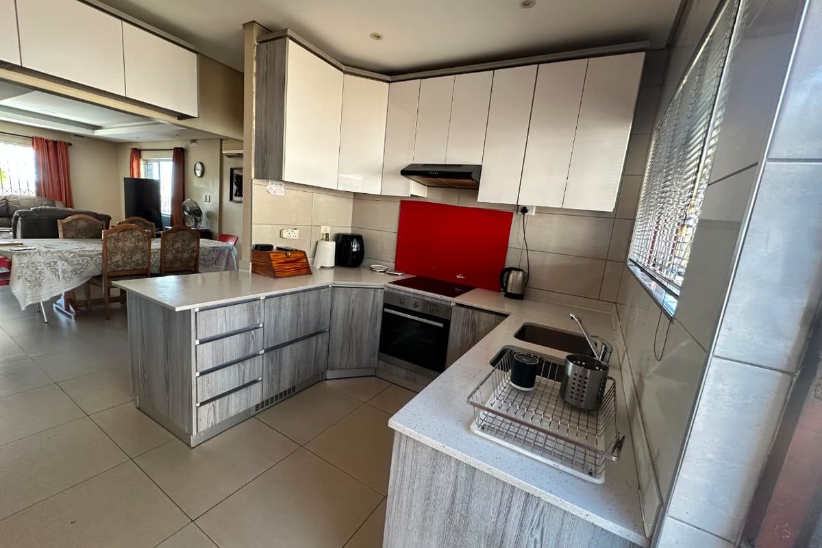 Modern kitchen featuring two-tone cabinetry, stone countertops, integrated appliances, and a vibrant red glass backsplash, seamlessly flowing into the adjacent dining area.