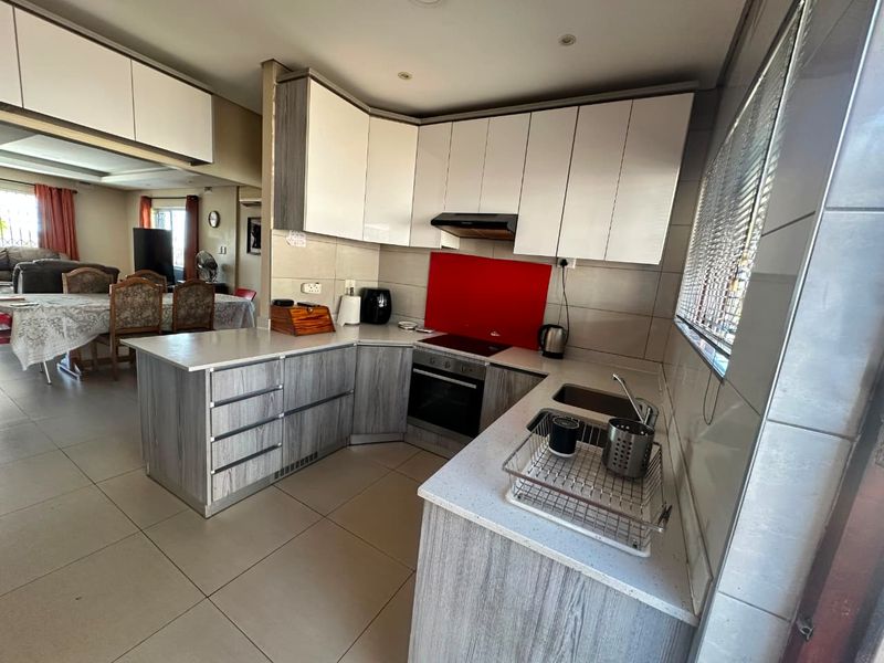 Modern kitchen featuring two-tone cabinetry, stone countertops, integrated appliances, and a vibrant red glass backsplash, seamlessly flowing into the adjacent dining area.