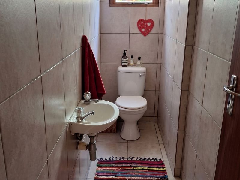 A compact guest bathroom featuring neutral ceramic wall and floor tiles, a wall-mounted basin, and a standard toilet with a window for natural light.