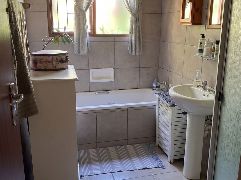 A functional bathroom featuring a bathtub, pedestal basin, and neutral wall and floor tiling, offering a clean and practical layout.