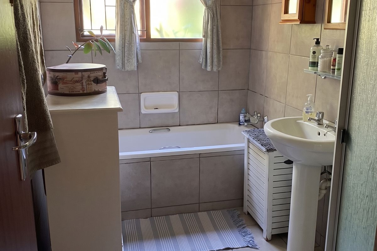 A functional bathroom featuring a bathtub, pedestal basin, and neutral wall and floor tiling, offering a clean and practical layout.