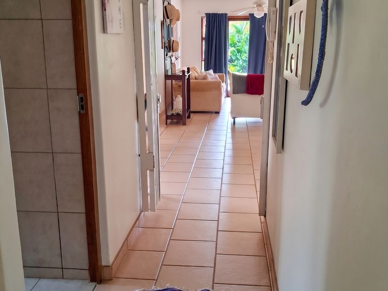 A tiled hallway providing access to the living area, featuring neutral wall finishes and a ceiling fan, connecting the interior spaces of the cottage.