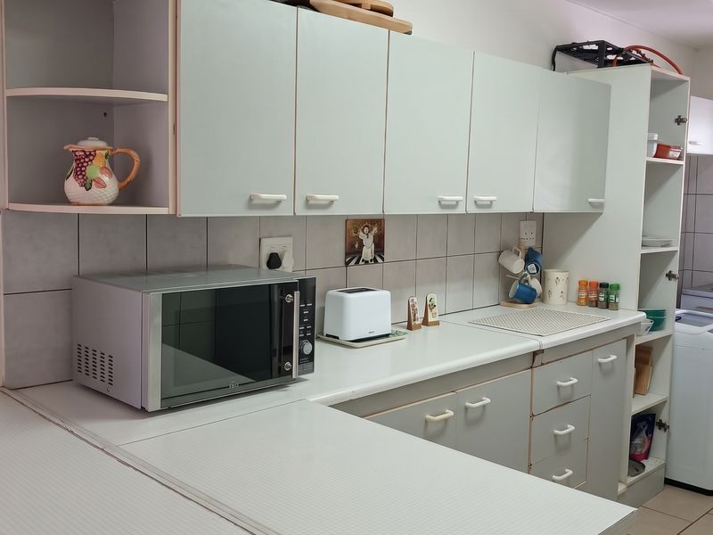 A functional kitchen featuring light-toned cabinetry, tiled backsplash, and ample counter space, showing signs of wear consistent with age.