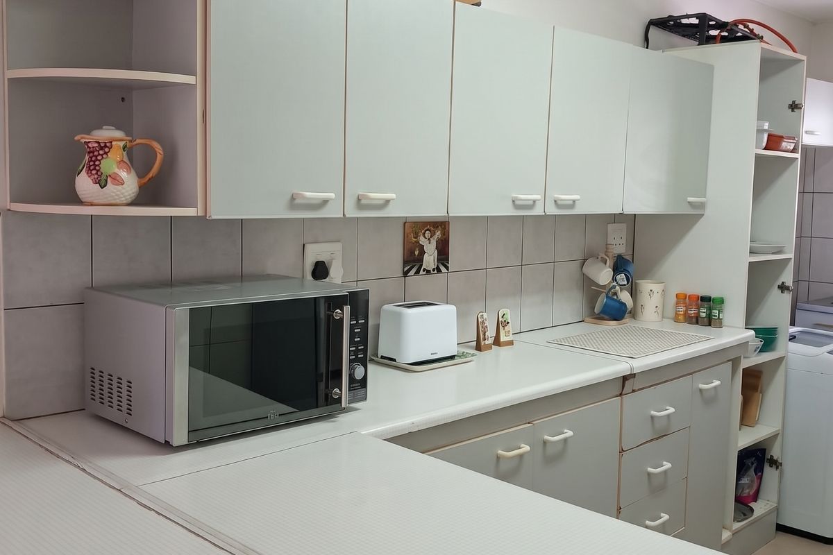 A functional kitchen featuring light-toned cabinetry, tiled backsplash, and ample counter space, showing signs of wear consistent with age.