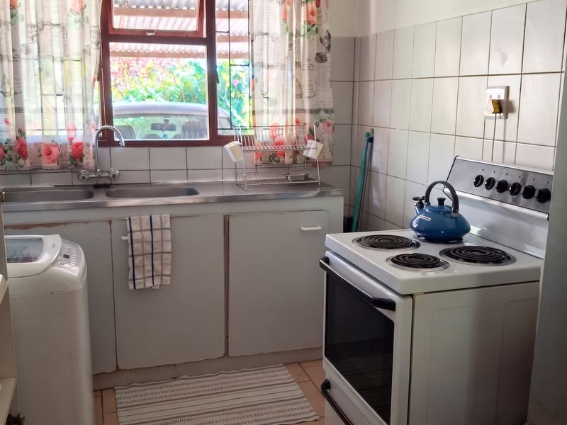 A functional kitchen featuring a stainless steel sink, tiled splashback, and a freestanding electric stove with ceramic floor tiles.