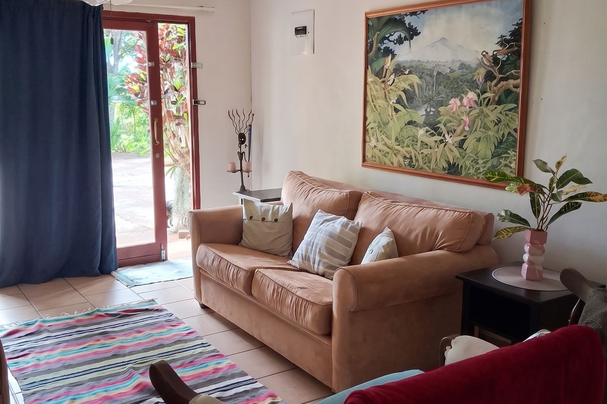 A cozy living room featuring tiled flooring, a ceiling fan, and direct access to the garden through a glass panel door.