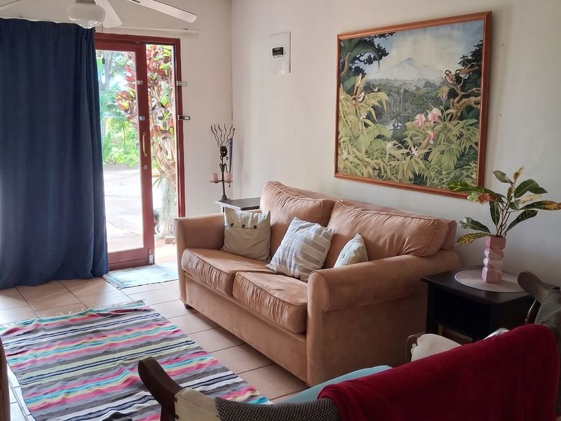 A cozy living room featuring tiled flooring, a ceiling fan, and direct access to the garden through a glass panel door.