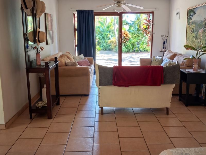 A living room featuring tiled flooring, a ceiling fan, and a sliding glass door providing access to the garden area.