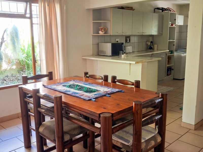 Open plan dining area adjacent to a functional kitchen with tiled flooring, ceiling fan, and direct access to the garden.