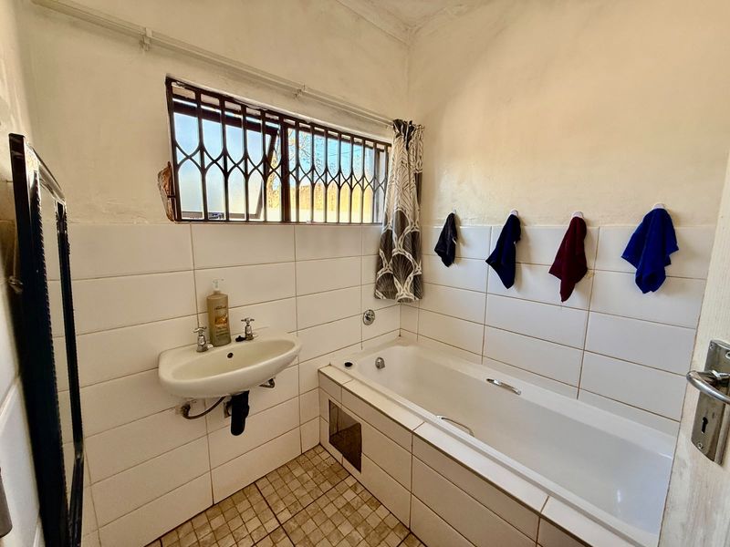 A functional bathroom featuring a built-in bathtub, wall-mounted basin, and tiled finishes, requiring some maintenance to the window area.