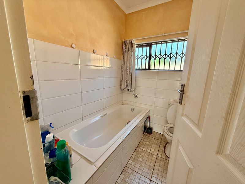 A compact bathroom featuring a built-in bathtub, toilet, and tiled finishes, requiring cosmetic updates to modernize the space.