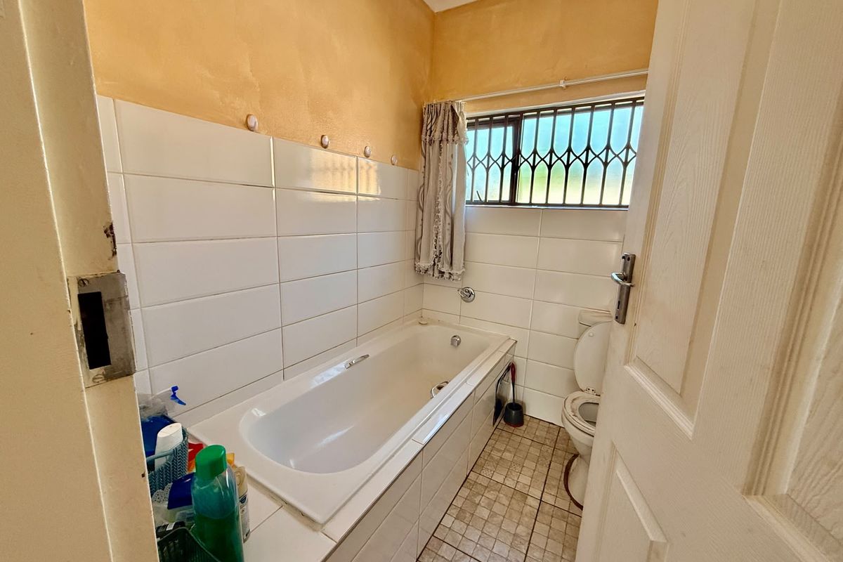 A compact bathroom featuring a built-in bathtub, toilet, and tiled finishes, requiring cosmetic updates to modernize the space.