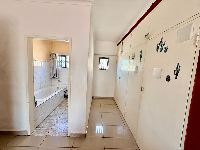 A hallway featuring extensive built-in storage cupboards and tiled flooring, providing direct access to an adjacent bathroom with a built-in bathtub.