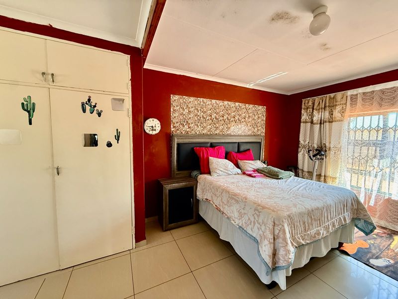 A bedroom featuring tiled flooring, built-in cupboards, and a security gate. The ceiling shows visible signs of water damage.