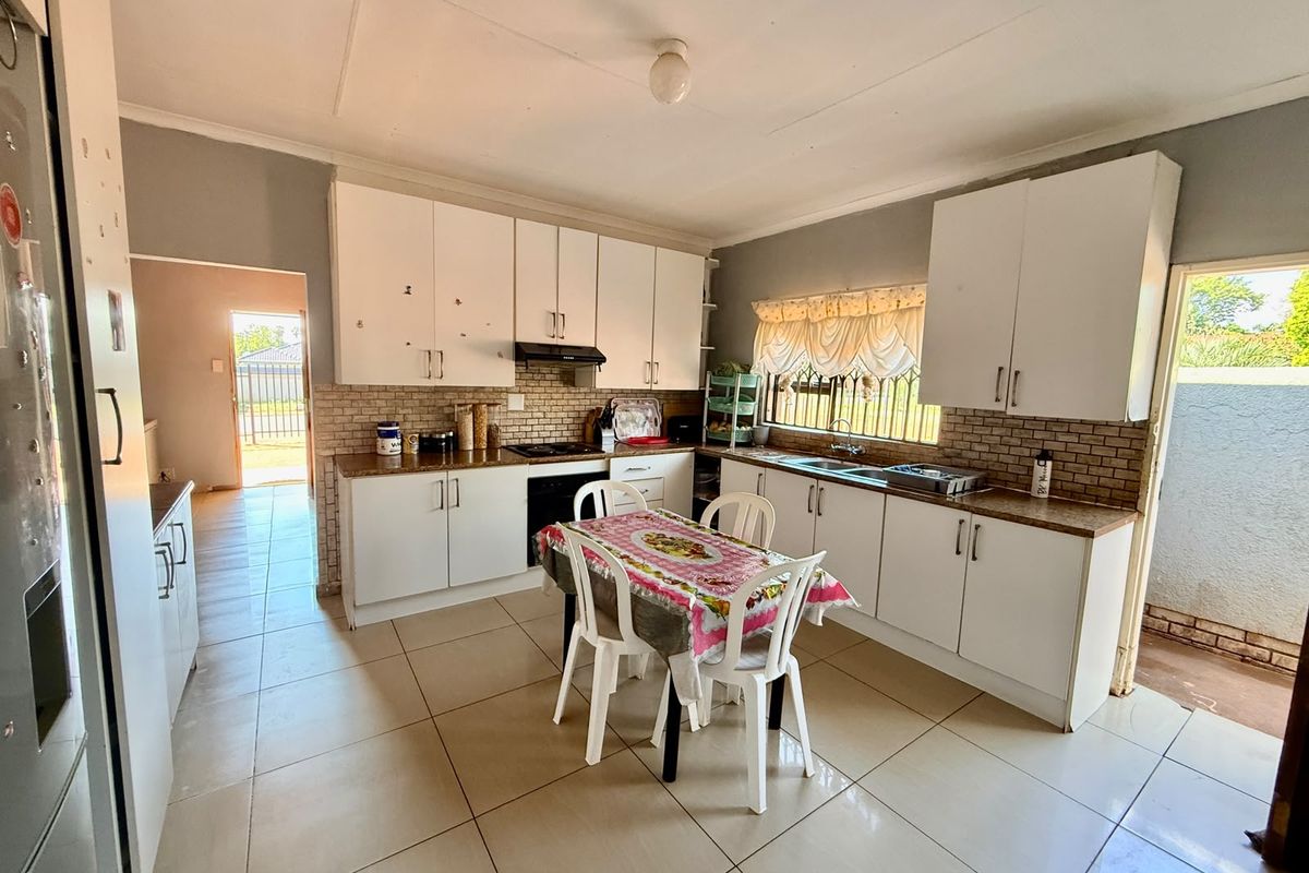 Functional kitchen featuring white built-in cabinetry, laminate countertops, tiled backsplash, and ceramic floor tiles with direct access to the exterior.