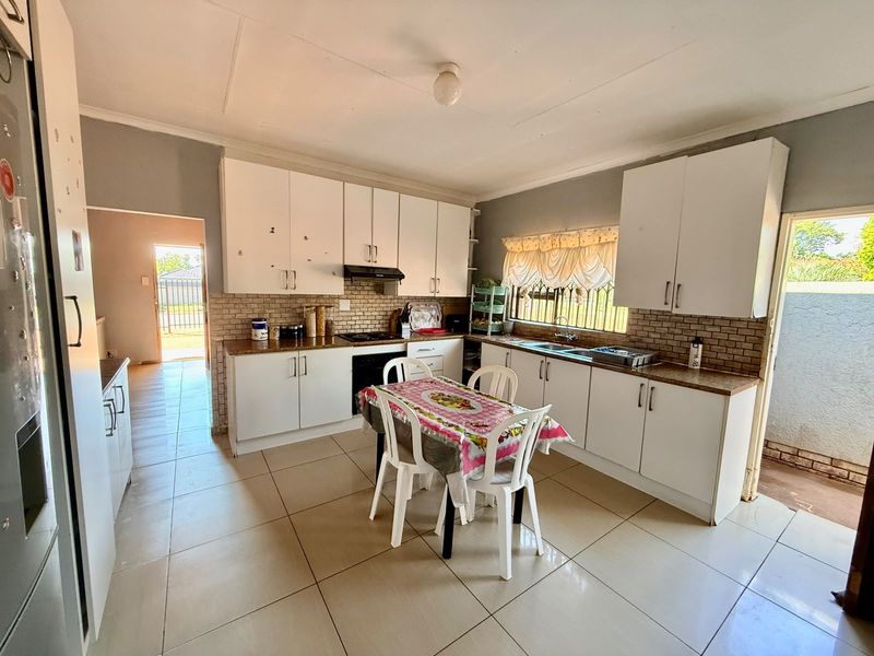 Functional kitchen featuring white built-in cabinetry, laminate countertops, tiled backsplash, and ceramic floor tiles with direct access to the exterior.